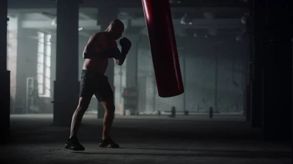 Hombre con saco de boxeo muscular en el gimnasio. Afro chico pateando bolsa de deporte — Foto de Stock