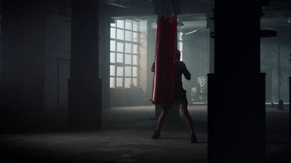 Kickboxer sporttáskát üt a tornateremben. Harcos boksz nehéz boxzsák kesztyűvel — Stock Fotó