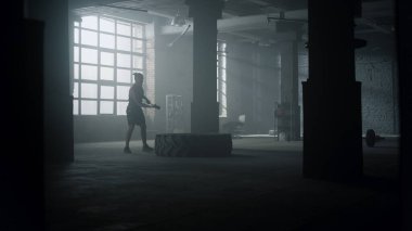 Adam güç çalışması için çekiç kullanıyor. Adam balyozla büyük lastiğe çarpıyor.