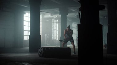 Spor kulübünde egzersiz yapan adam. Büyük lastikleri çekiçle döven adam.