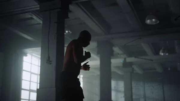 Homem atlético a treinar boxe no edifício do sótão. Boxer masculino lutando com sombra — Fotografia de Stock