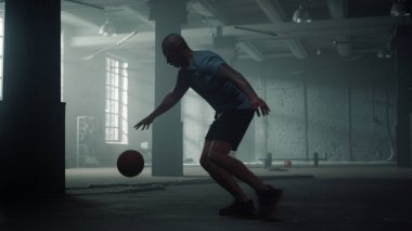 Basketbolcu spor kulübünde top sektiriyor. Sporcu spor salonunda top sürüyor.