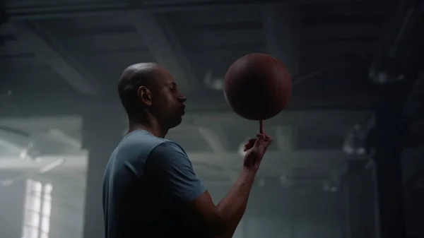 Porträt eines ernsthaften Basketballspielers, der in der Turnhalle einen Basketballball auf dem Finger dreht — Stockfoto