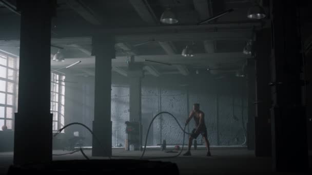Kerl kämpft in der Turnhalle gegen Seile. Sportlicher Mann beim Crossfit-Training im Dachgeschoss — Stockvideo