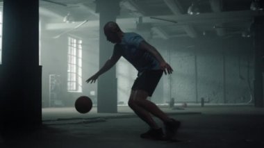 Basketbolcu spor kulübünde top sektiriyor. Sporcu spor salonunda top sürüyor.