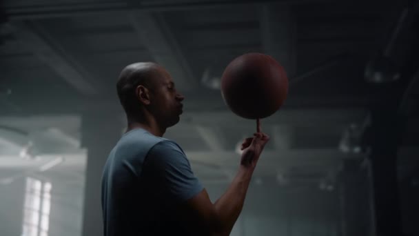 Портрет серьезного баскетболиста, вращающего баскетбольный мяч на пальце в спортзале — стоковое видео