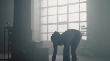 Spor kadını ağır halterlerle egzersiz yapıyor. Kadın hamlelerle çömeliyor.