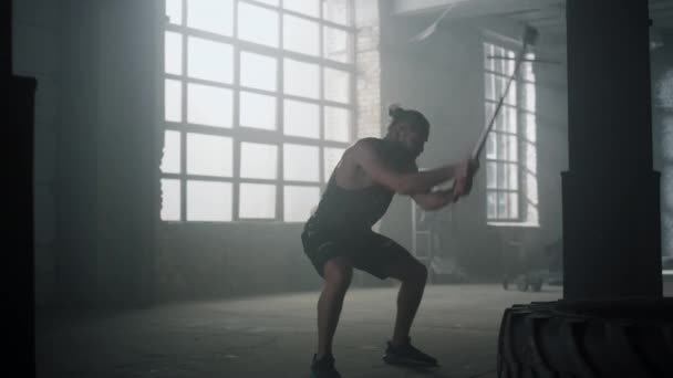 Sportowiec uderza w oponę młotkiem w siłowni. Mężczyzna ćwiczący z młotem kowalskim — Wideo stockowe