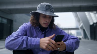 Açık havada cep telefonu kullanan bir hipster. Adam caddede akıllı telefon kaydırıyor..