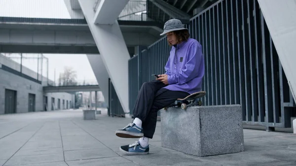 Tarz sahibi bir adam dışarıda telefon ekranı arıyor. Skater akıllı telefondan mesaj yazıyor. — Stok fotoğraf
