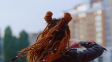 Kızıl saçlı kadın dışarıda dans ediyor. Kentsel arka planda gezinen aktif kız