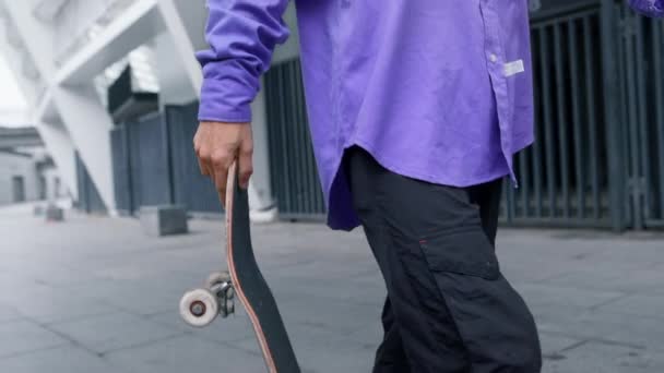 Mano de hombre sosteniendo tablero afuera. Hipster irreconocible caminando por la calle de la ciudad. — Vídeo de stock
