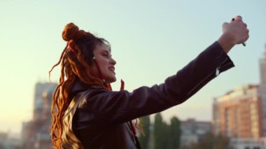 Şık bir kadın dışarıda cep telefonuyla selfie çekiyor. Telefon kamerası için poz veren kız.