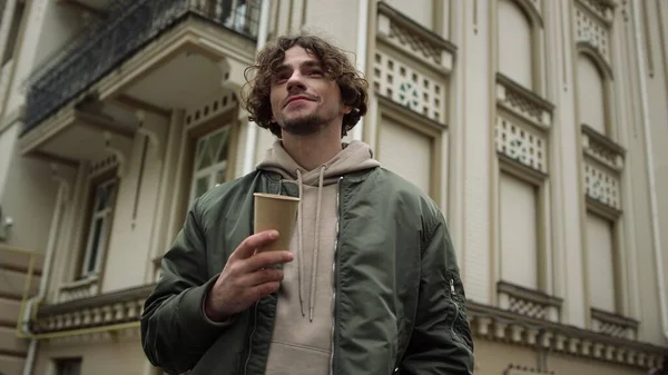 Hombre feliz con café con leche sonriendo al aire libre. Chico alegre sosteniendo taza de papel en la calle. — Foto de Stock