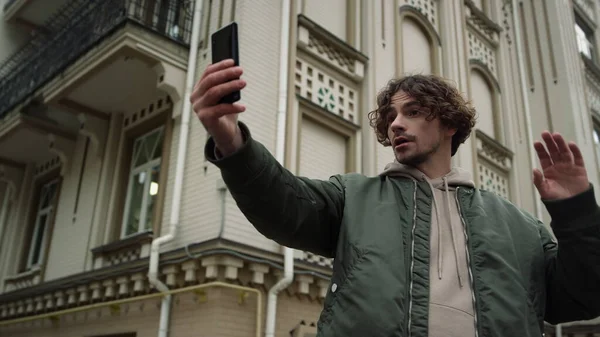 Hombre joven usando el teléfono para videollamada al aire libre. Tipo saludando de la mano a la cámara en la ciudad. — Foto de Stock