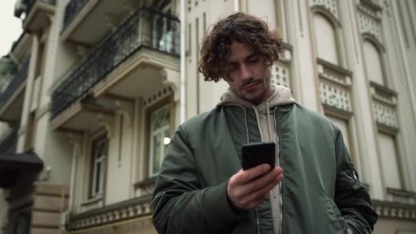 Homme concentré textos sur smartphone en plein air. Positif hipster tenant téléphone portable. — Video