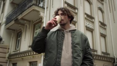 Şehir sokağında latte içen odaklanmış bir adam. Ciddi bir adam dışarıda kahve tutuyor..