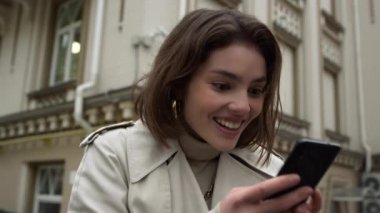 Dışarıdaki telefondan mesaj okuyan heyecanlı bir kadın. Şehirde cep telefonu tutan bir kız..