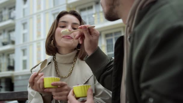 Pareja feliz disfrutando de helado al aire libre. Hombre alimentando a mujer en calle urbana. — Vídeos de Stock