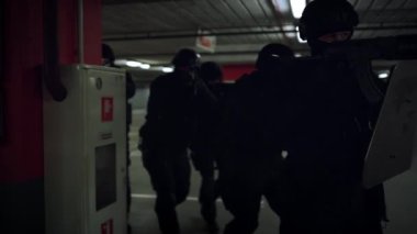 Bir grup SWAT üyesi ellerinde silahlarla yeraltı otoparkında yürüyor.