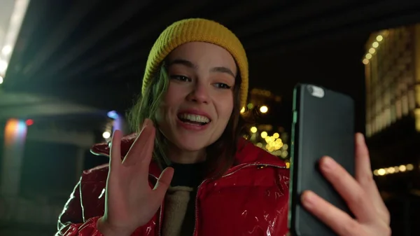 Mulher alegre usando celular para videochamada na rua da cidade à noite. — Fotografia de Stock