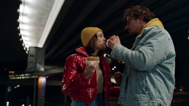 Neşeli çift dışarıda eğleniyor. Kadın ve erkek şehirde hamburgerle oynuyorlar..