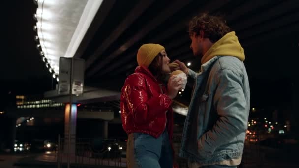 Pozytywna para jedząca przekąski w nocy. Mężczyzna karmienie kobiety pod mostem. — Wideo stockowe