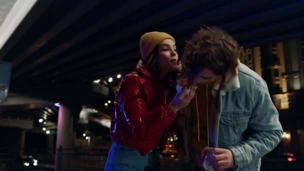 Glada par kysser på stadens gata. Man biter av kvinna hamburgare utomhus. — Stockvideo