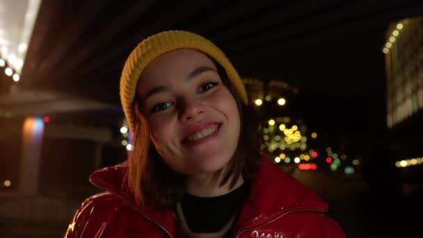 Fröhliche Frau mit Blick auf die Lichter der Stadt im Freien. Hübsches Mädchen lächelt auf der Straße. — Stockvideo