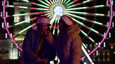 Sokak ortasında gülen bir çift. Noel Baba şapkaları giyin, dışarıda eğlenin..