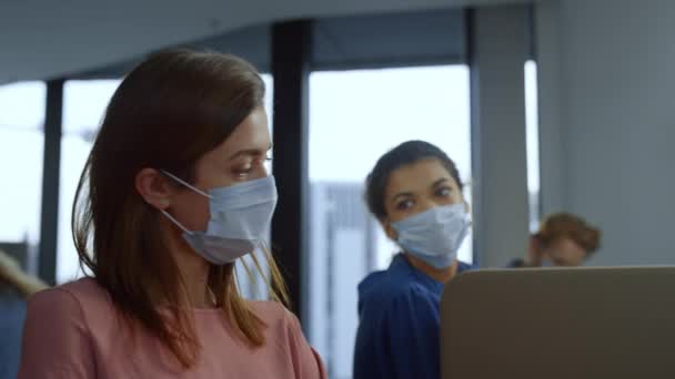 Mujer de negocios enfocada en máscara médica en la cara de trabajo en el ordenador portátil en la oficina — Vídeos de Stock