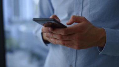 İş adamı elleri cep telefonundan mesaj yolluyor. Yakın plan genç adam telefon kullanıyor.