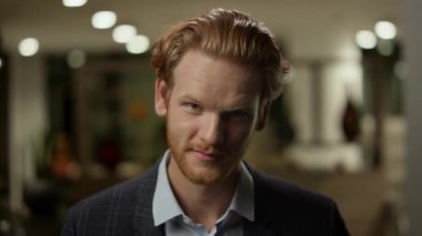 Ofiste kameraya bakan kendine güvenen bir iş adamı. Kızıl saçlı adam kameraya poz veriyor.