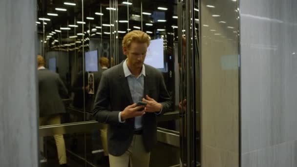 Hombre de negocios serio usando smartphone en ascensor. Administrador escribiendo en el teléfono móvil — Vídeo de stock