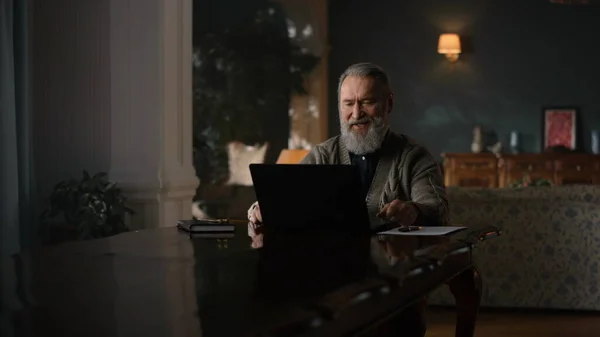 Happy old man having video call laptop luxury interior. Senior man using laptop