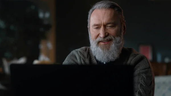 Hombre viejo barbudo que tiene una computadora de video llamada en el interior. Hombre de negocios senior usando pc. —  Fotos de Stock