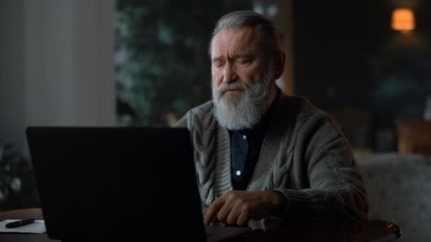 Сосредоточенный старший мужчина разговаривает во время видеозвонка на ноутбуке — стоковое видео