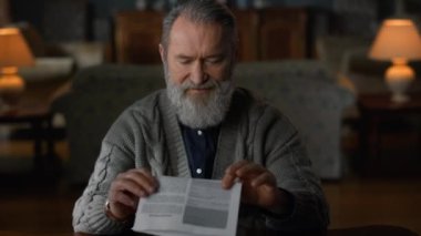 Yaşlı adam lüks oturma odasında belge okuyor. Düşünceli kıdemli adam.