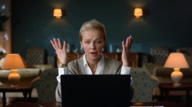 Sinirli yaşlı kadın laptop bilgisayarında eski moda dolapta video görüşmesi yapıyor.
