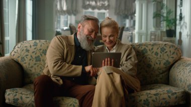 Mutlu yaşlı çift dijital tablet bilgisayar kullanarak gevşeyerek konuşuyor.
