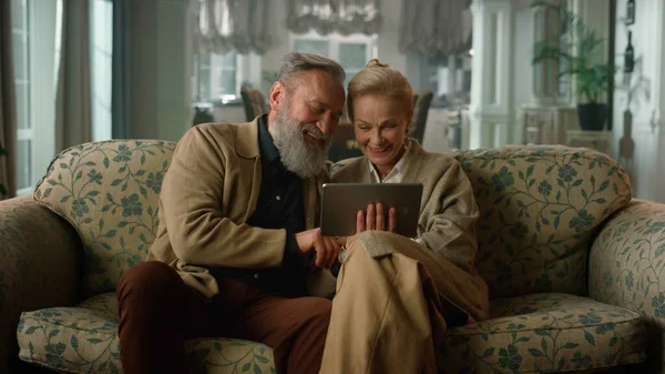 Lykkelig eldre par som snakker avslappende ved hjelp av digital nettbrett stockfoto