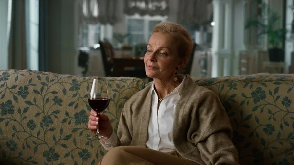 Mulher madura sonhadora degustando copo de vinho tinto na sala de estar vintage. Mulher idosa — Fotografia de Stock