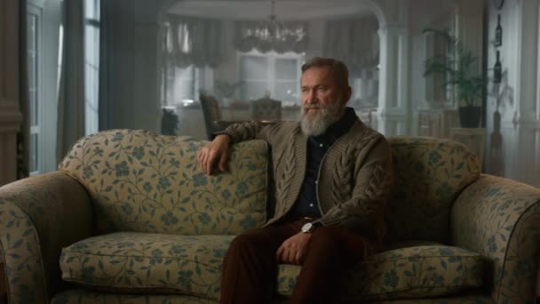 Schöner älterer Herr denkt an Sofa im gemütlichen Wohnzimmer. Wohlstandsweisheit Gelassenheit — Stockvideo