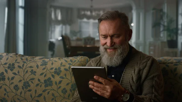 Hymyilevä vanha mies lukee uutisia verkossa tabletti tietokone. Happy vanhempi mies käyttää pad — kuvapankkivalokuva