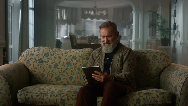 Спокойный пожилой человек с планшетным компьютером на диване. Пенсионный дед — стоковое фото