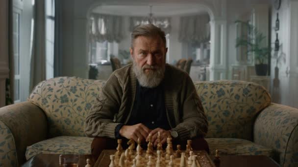 Pozorný starší muž si myslí, že šachová partie je doma. Starší hráč hraje šachy — Stock video