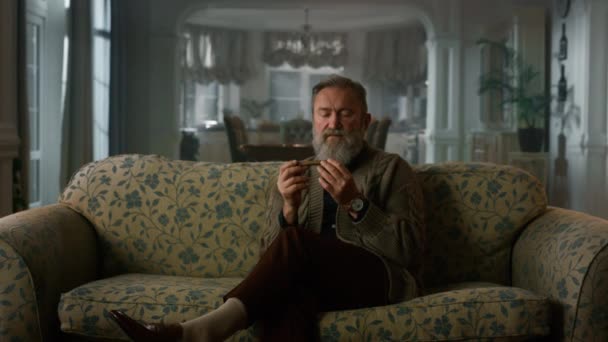 Расслабленный старший джентльмен, нюхающий кубинскую сигару. Богатый старик расслабляющий диван — стоковое видео