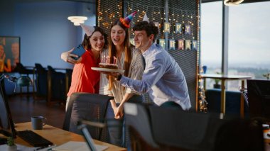 Doğum günü pastası tutan arkadaşlar ofiste kutlama yaparken selfie çekiyorlar. Şirket partisinde eğlenen neşeli insanlar. Şapkalı enerjik meslektaşlarımız kutlama zamanını hatırlıyor.