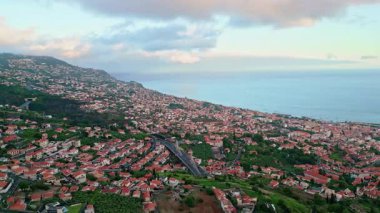 İnsansız hava aracı kıyı kasabası bulutlu gökyüzünün altında dağ yamaçlarına kurulmuş. Teraslı tepeler ve muhteşem mavi okyanus sularına bakan yeşil alanlar. Resimli, yemyeşil kırsal araziye yerleştirilmiş manzara köyü