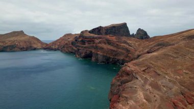 Mavi okyanus tarafından yıkanan insansız hava aracı muhteşem okyanus kayaları. Sakin deniz kayalıkları uçsuz bucaksız denizle çelişiyor. Dalgalanan su bulutlu gökyüzünde volkanik oluşumu yıkıyor. Açık deniz manzaralı sakin bir yer.